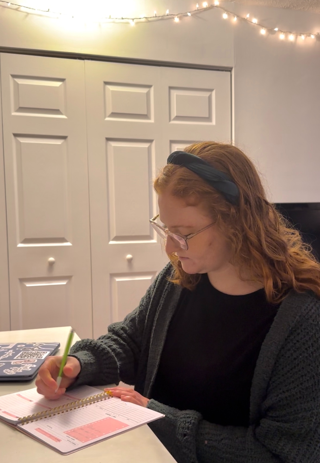 red haired woman sits at desk, writing in planner