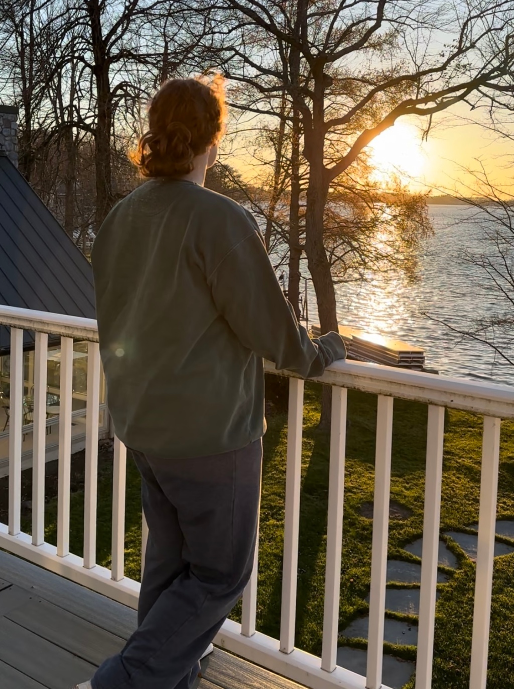 woman stands on a balcony and looks out at the sunset over a lake